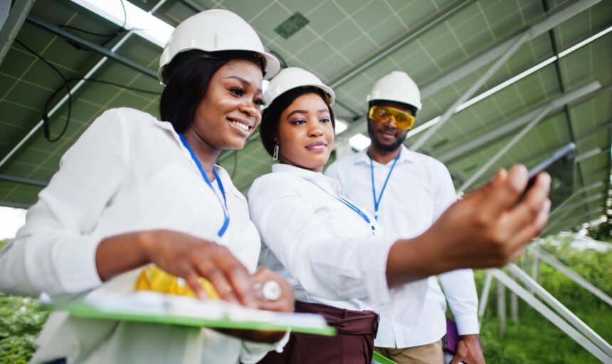 African american technician checks the maintenance of the solar panels. Group of three black engineers meeting at solar station. Make selfie by phone.